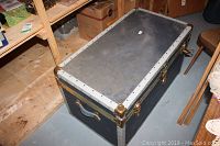 Top and side views of the vintage steamer trunk showing metal clasps, white metal trim, brass corner protectors, and leather handles on each end.
