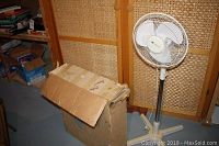 Westinghouse electric standing fan with adjustable height next to a worn cardboard box containing the Torcan fan.