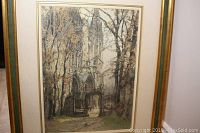 Framed etching showing Chartres Cathedral surrounded by trees with autumn leaves, gold-toned frame with pale blue inner border and off-white matting
