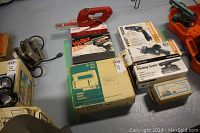 Photo showing Rockwell jig saw kit box, Weller soldering gun kit in case with box, Homelite cordless trimmer, Black & Decker drill, saw and finishing sander boxes, and some cords
