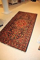Photo showing full view of wool rug with floral pattern and cut fringe on the near edge.