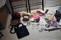 Overall view of all jewelry, handbags, scarves, wallets, and pantyhose displayed on carpet.