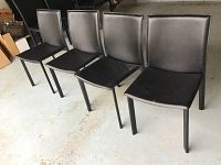 Four black vinyl covered chairs arranged in a row showing their side and front profiles.