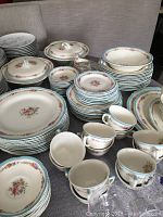Overall view of the earthware dishes set arranged on table showing plates, cups, and covered dishes with floral and blue trimmed pattern.