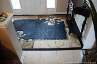 Front entrance area carpet laid out on tiled floor, visible edge threading and staining on beige border and some wear on blue field.