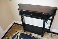 Front and top angled view of the black wooden hall table showing drawer and turned legs.