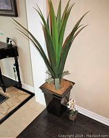 Large faux green plant with long pointed leaves in tall dark rectangular planter with faux moss.