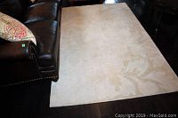 Full view of cream wool carpet on hardwood floor, showing overall appearance and size next to leather sofa.