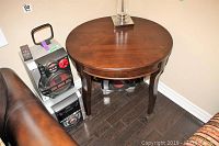 Round wooden side table adjacent to a couch and audio speaker system, showing overall structure and finish.