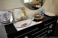 Overview of boxed chargers - gold and silver sets, Joshua Maxwell platter box, lidded blue and white ginger jar, star-shaped plates, napkin rings and cloth napkins on black dresser.