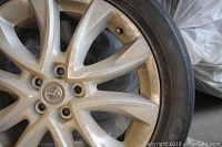 Close-up of Mazda alloy rim showing wear and dirt on rim and tire sidewall.