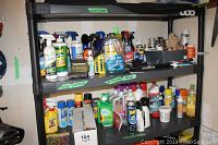 Shelving unit with various cleaning sprays, car waxer kit bottle, bug sprays, and other household products.