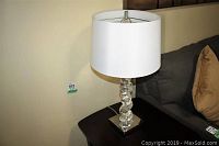 Full view of one acrylic table lamp on dark wood table next to a gray sofa, showing white drum shade and acrylic body.