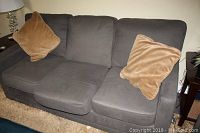Front angle showing full gray sofa with two beige square throw pillows on the ends, minor staining on cushions visible