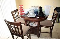 Photo showing round wooden table with dark finish and the four upholstered padded chairs around it, with various kitchen items on the table.