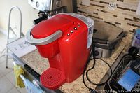 Red Keurig K-Compact K35 single cup coffee maker on a kitchen counter with water reservoir visible.