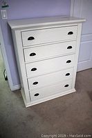 Front view of the white five-drawer highboy dresser showing black handles and surface wear.