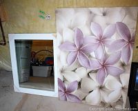 Photo showing the beveled mirror with white frame leaning against a wall next to the floral canvas art.