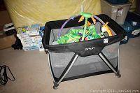 Image showing the Nuna black play pen with mesh sides and educational floor mat with toys inside.