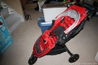 Three-quarter view of red stroller showing front wheel and chassis