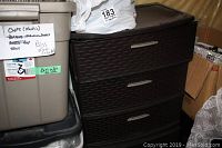 Dark brown woven-pattern plastic three-drawer unit seen alongside storage bins. Drawers appear filled with items.