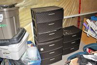 Three dark brown resin 3-drawer storage units placed in basement storage. Various plastic bins surround them. Drawers are slightly open and some dust visible.