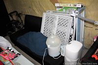 Wide angle photo showing assorted baby and child safety products including Diaper Genie, bottle sterilizer, baby gates, bed rails, and Jolly Jumper seat arranged on and near a black futon sofa.