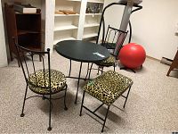 Bistro style black metal framed table with round laminated top and two chairs with leopard print upholstered seats plus bench.