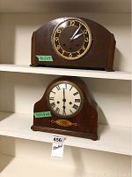Side view and front view photo of two vintage mantle clocks stacked on shelf, showing overall shape, dial, and condition.