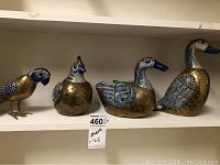 Full set of four decorative metal wildlife figurines displayed on shelf showing parrot, quail, and two ducks