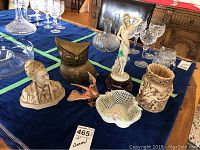 Table display showing statue, brass owl, Belleek basket, carved vase, glass bird figurine and assorted clear glassware on navy cloth.