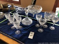 Eleven Waterford crystal pieces displayed on a blue cloth with five matching wine glasses, a decanter with stopper, a large footed bowl, and four additional stemware glasses.