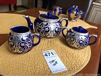 Photo of blue and silver tea set with teapot, sugar bowl, and creamer on a woven placemat.