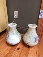 Pair of onyx vases displayed on wooden floor near wall outlet.