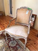 Front angled view of vintage upholstered wooden accent chair with distressed painted frame and beige velour fabric.