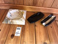 Three onyx ashtrays displayed on wood surface: one round beige and brown veined onyx ashtray on square base, two dark oblong onyx ashtrays.