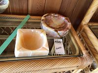 Two onyx ashtrays on a glass and rattan shelf, round and square shapes shown.