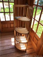 View of the plant stand from an angle showing all four curved shelves and the hinge allowing it to fold.