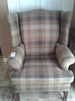 Front view of beige and brown plaid wingback armchair showing rolled arms and cushioned seat.