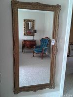 Full length gold-colored ornate mirror standing in a room reflecting furniture