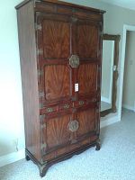 Front view of tall wooden cabinet showing wood grain panels and decorative metal hardware.
