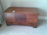 Front and angled view of cedar chest showing wood grain panels and drawer with handles.