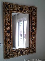 Front view of rectangular mirror on wall showing gold and black carved ornate frame detail