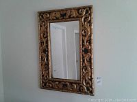 Front view of large rectangular mirror with carved gold-colored frame and black background.