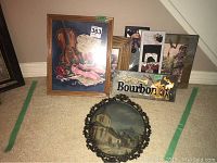 Seven framed art pieces including a framed tapestry, a metal bourbon sign, and multiple framed paintings and prints arranged on the floor.