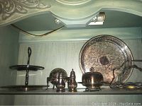 Display of silver-plated serving ware including trays, covered dishes, shakers and tiered stand on shelf showing size, design and condition.