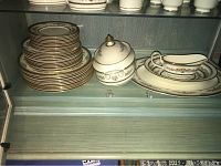 Full view of the stacked Minton fine bone china plates alongside covered and uncovered vegetable bowls and gravy boat with tray in a cabinet.