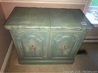 Front view of the greenish-blue wooden buffet showing scalloped edges, decorative panels on doors, and brass ring pulls.
