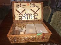 Open wicker picnic basket showing cutlery, plates, salt and pepper shakers inside lid and basket base