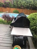 Side view of Vermont Castings barbecue showing blue lid, stainless steel side table, and lower shelf.